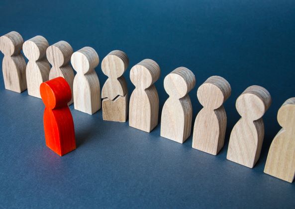 Figuras de madera simulando personas, diez de color madera y una roja 